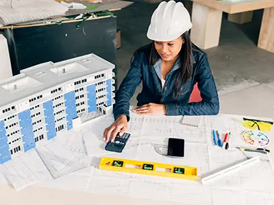 Civil engineer preparing bar bending schedule BBS with building drawings and calculator in Ahmedabad.